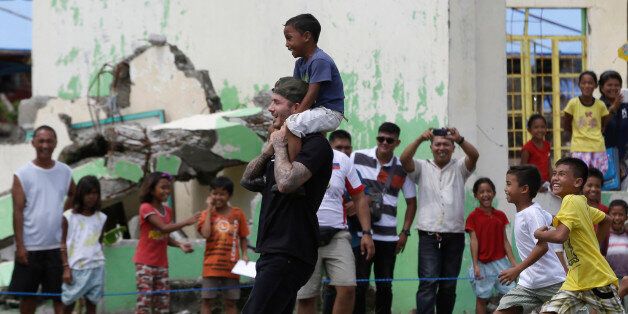 Former England soccer team captain David Beckham carries a boy on his shoulders as he plays soccer with young typhoon-survivors during his visit to typhoon-ravaged Tanauan township, Leyte province in central Philippines Friday, Feb. 14, 2014. Beckham, who spent the Valentine's Day with typhoon survivors, was one of several international celebrities to raise funds for typhoon victims. (AP Photo/Bullit Marquez)