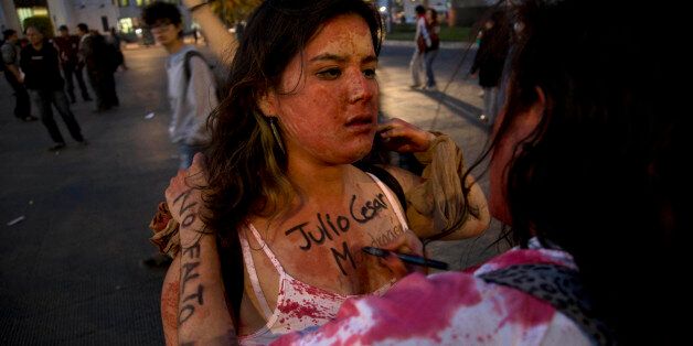 A protester gets the name of Julio Cesar Mondragon, a student that was savagely killed on the day that 43 students went missing, painted on her chest as she participates in a march in Mexico City,Monday, Dec. 1, 2014. Protesters marched in several cities in Mexico on Monday to mark the second anniversary of President Enrique Pena Nieto's administration and demand the government find 43 students who disappeared at the hands of police. (AP Photo/Eduardo Verdugo)