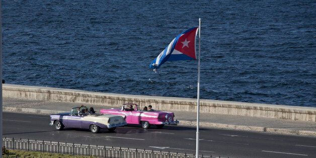 Tourists ride in a classic American car on the Malecon in Havana, Cuba, Wednesday, Dec. 17, 2014. After a half-century of Cold War acrimony, the United States and Cuba abruptly moved on Wednesday to restore diplomatic relations _ a historic shift that could revitalize the flow of money and people across the narrow waters that separate the two nations. The U.S. is easing restrictions on travel to Cuba, including for family visits, official government business and educational activities. But tourist travel remains banned. (AP Photo/Desmond Boylan)
