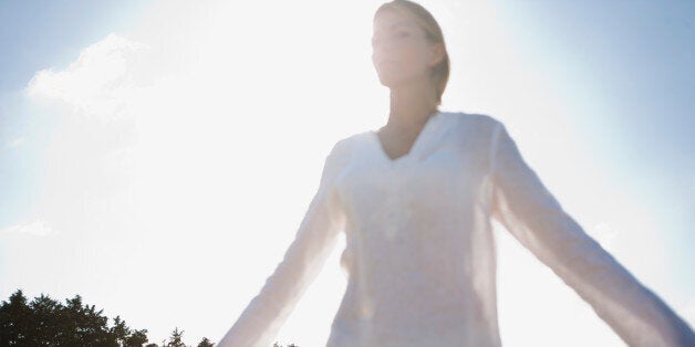 Mid-adult woman standing in field with eyes closed and arms outstretched