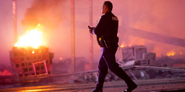 A police officer walks by a blaze, Monday, April 27, 2015, after rioters plunged part of Baltimore into chaos, torching a pharmacy, setting police cars ablaze and throwing bricks at officers. (AP Photo/Matt Rourke)