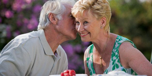 67 year old man gives woman a kiss on the cheek while enjoying tea and cake in the garden.