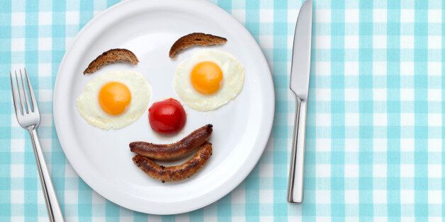 A plate of fried breakfast arranged as a smiling face on a white plate sitting on a blue gingham tablecloth.