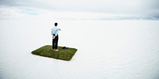 Businessman standing on small grass island in large body of water looking out