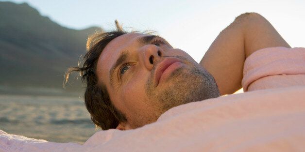 portrait of young man lying on beach looking worried