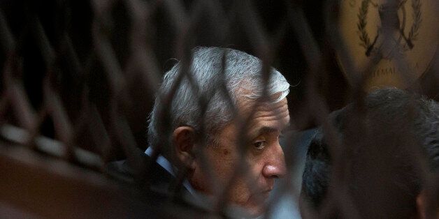 Guatemala's former president Otto Perez Molina, photographed through a window, sits in court for a third hearing on corruption allegations that led him to resign, in Guatemala City, Tuesday, Sept. 8, 2015. The court is considering allegations that Perez Molina was involved in a scheme in which businesspeople paid bribes to avoid import duties through Guatemala's customs agency. (AP Photo/Esteban Felix)