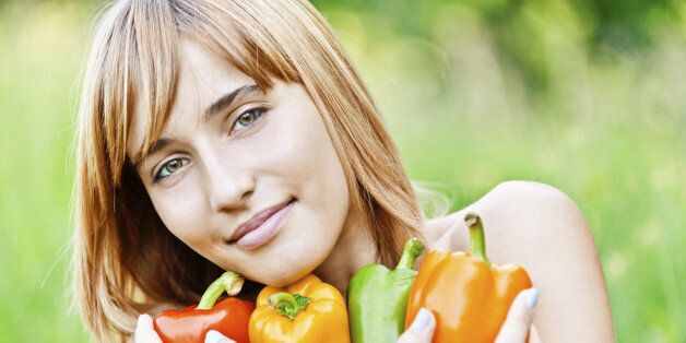 Young beautiful woman holds multi-colored Bulgarian pepper in arm and smiles, against summer green nature.