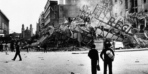 People inspect the damaged Hotel Regis after an earthquake, registering 7.8 on the Richter scale, hit Mexico City on Thursday, Sept. 19, 1985. A policeman, at left, patrols the street to aid injured and minimize looting in the populous capital. (AP Photo/Paul Conklin)