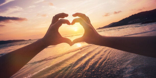 Couple formed heart shape with their hands against sunset over the horizon.