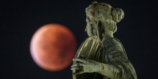 A so-called 'blood moon' can be seen behind a statue during a total lunar eclipse in Frankfurt am Main, western Germany, on September 28, 2015. Skygazers were treated to a rare astronomical event when a swollen 'supermoon' and lunar eclipse combined for the first time in decades, showing Earth's satellite bathed in blood-red light. AFP PHOTO / DPA / FRANK RUMPENHORST +++ GERMANY OUT (Photo credit should read FRANK RUMPENHORST/AFP/Getty Images)