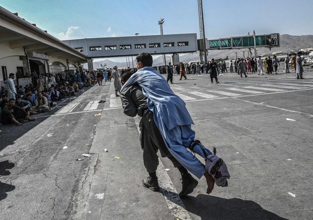 A volunteer carries an injured man as other people can be seen waiting at the Kabul airport on August...