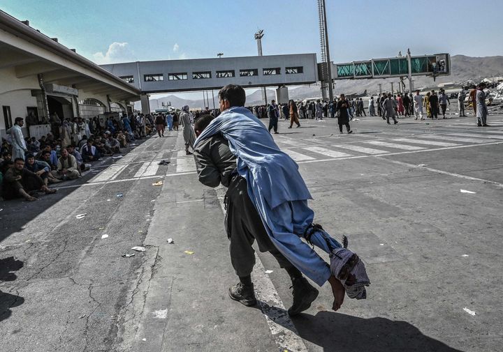 A volunteer carries an injured man as other people can be seen waiting at the Kabul airport on August 16, 2021
