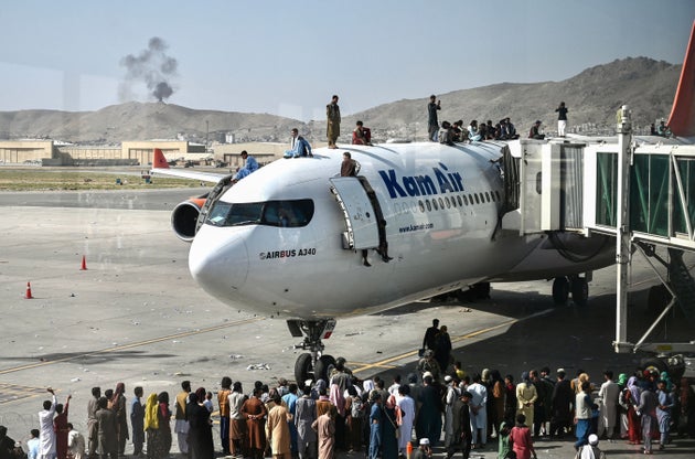 Afghan people climb atop a plane as they wait at the Kabul airport in Kabul on August 16,