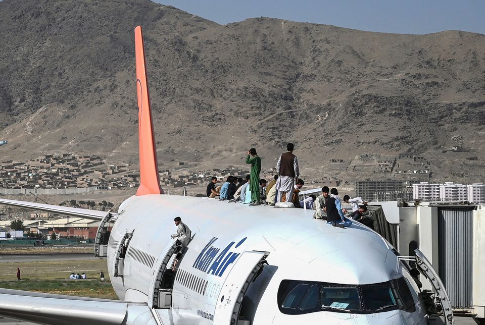 Afghan people climb atop a plane as they wait at the Kabul airport in Kabul on August 16,