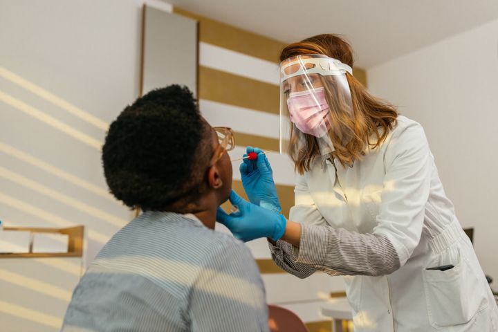 Doctor in a protective suit taking a throat swab from a patient to test for possible coronavirus infection (a PCR test)