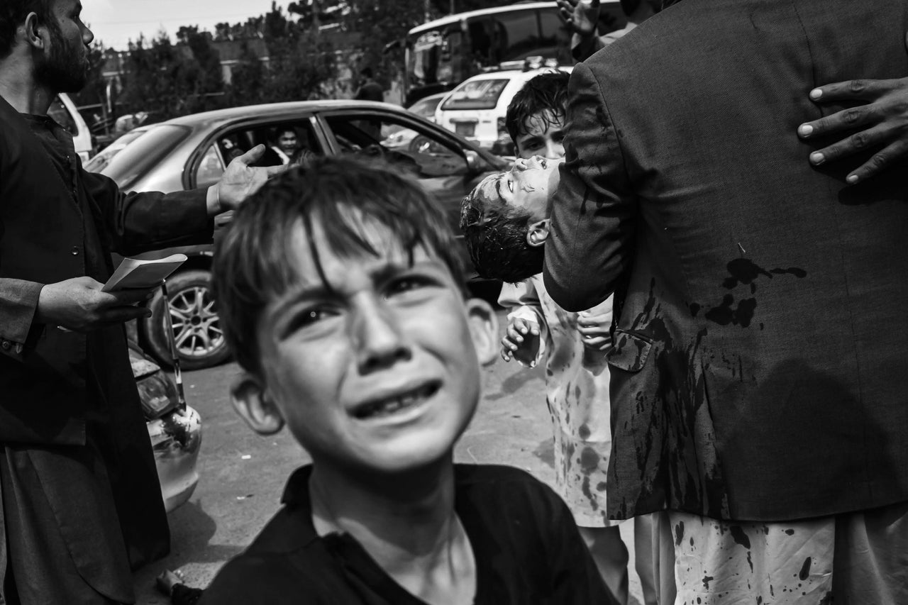 A man carries a bloodied child on Tuesday as a woman lies wounded on the street after Taliban fighters use guns, whips, sticks and sharp objects to maintain crowd control over thousands of Afghans who continue to wait outside the airport in Kabul for a way out.
