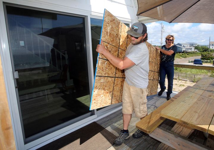 James Masog, center, and Gary Tavares, right, move particle board into place to board up the sliding glass doors of a client's house in Charlestown, R.I., ahead of Henri, Saturday, Aug. 21, 2021. (AP Photo/Stew Milne)