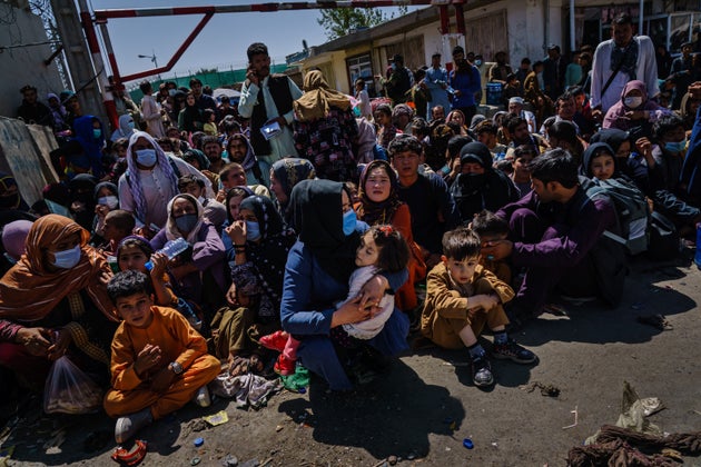 Women and children are made to crouch and wait outside the Taliban controlled check point near the airport's...