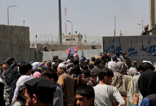 US soldiers stand inside the airport wall as hundreds of people gather near an evacuation control checkpoint...