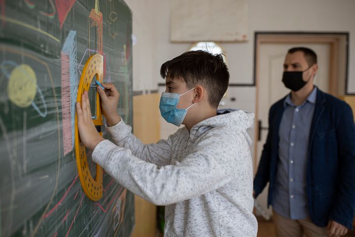 The teacher with the protective mask talks to the students about how to solve the mathematical equation