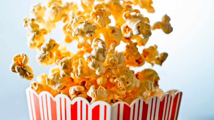 Close up of overflowing popcorn from red striped carton against blue background.