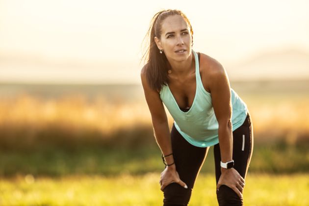 Fit sportswoman rests with hands on legs after a workout outdoors on a late summer afternoon.