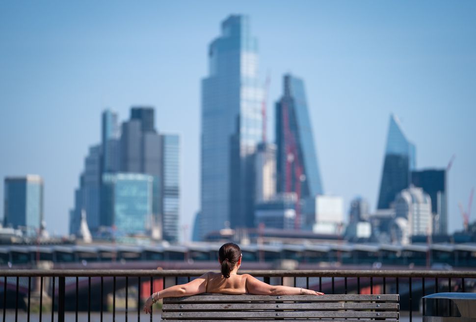 A woman soaks up the sun on the South Bank, London, looking out at the view of Blackfriars Bridge and skyscrapers in the City financial district. 