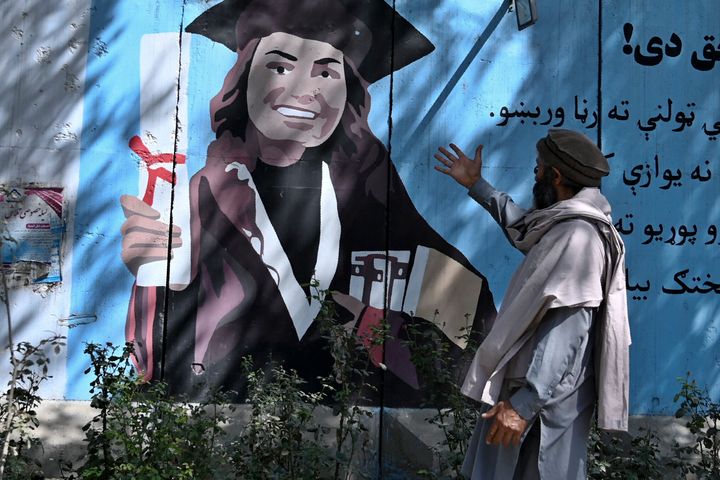 Ένας άντρας κάνει χειρονομίες καθώς περνάει από τοιχογραφία που απεικονίζει μια φοιτήτρια έξω από το Υπουργείο Ανώτατης Εκπαίδευσης του Αφγανιστάν στην Καμπούλ