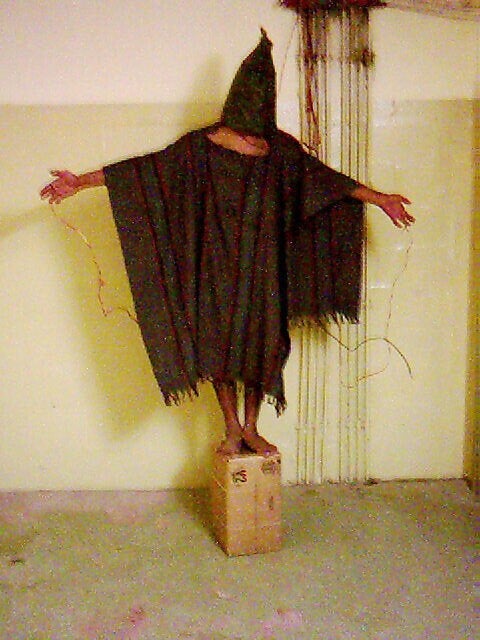An unidentified detainee is forced to stand on a box with a bag over his head and wires attached to him in late 2003 at the A