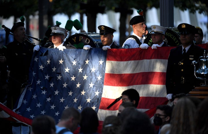 New York police and firefighters hold a U.S. flag as a band plays the US National Anthem at the National 9/11 Memorial during a ceremony commemorating the 20th anniversary of the 9/11 attacks.