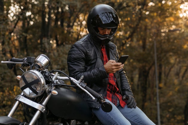 Caucasian male biker sitting on his motorbike and using his smart phone