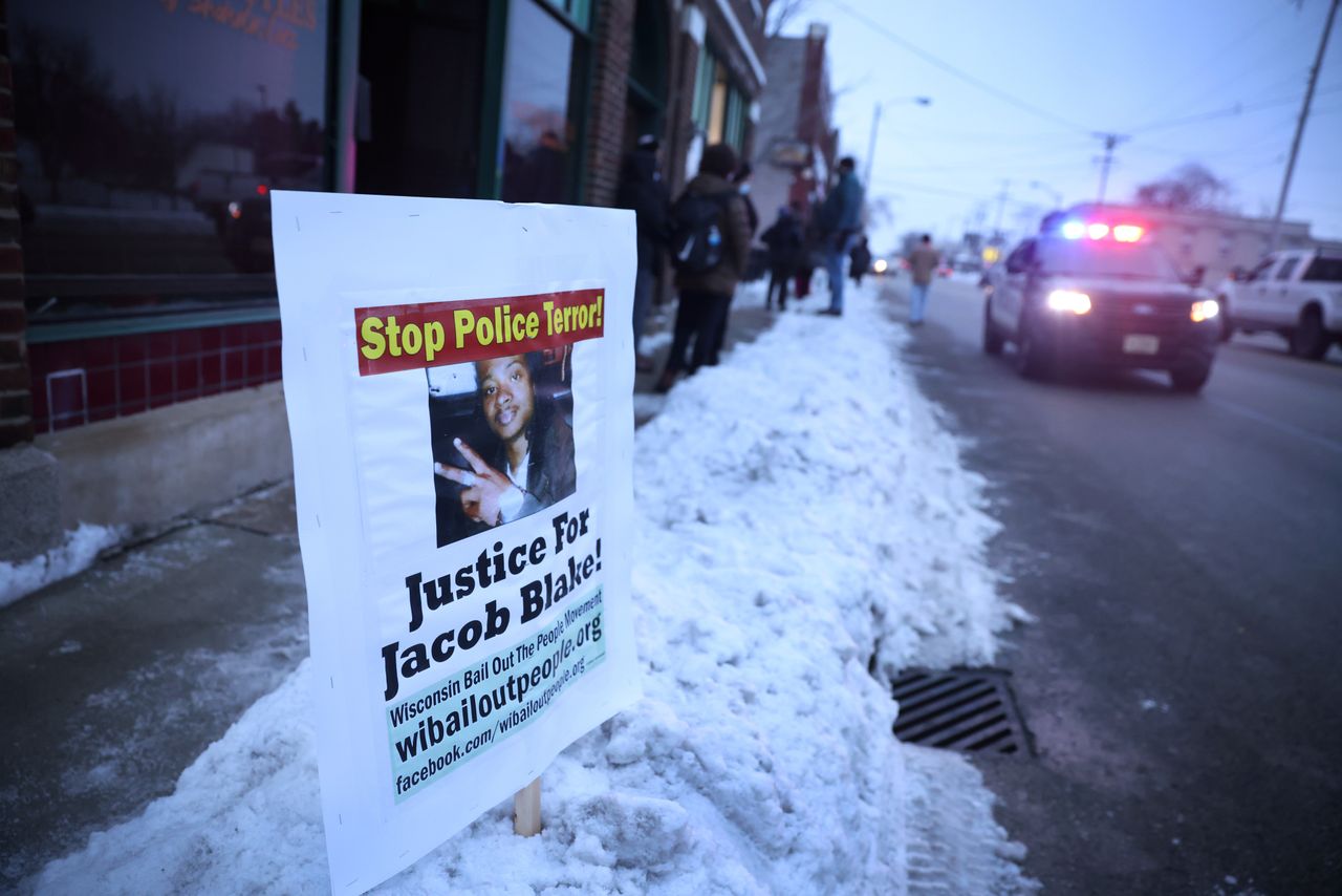A police car drives past a sign showing support for Jacob Blake Jr., who was shot seven times in the back by a Kenosha police officer on Aug. 23, 2020. Blake was left paralyzed from the waist down.