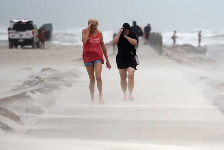 People shield their faces from wind and sand ahead of Tropical Storm Nicholas, Monday, on the North Packery Channel Jetty in