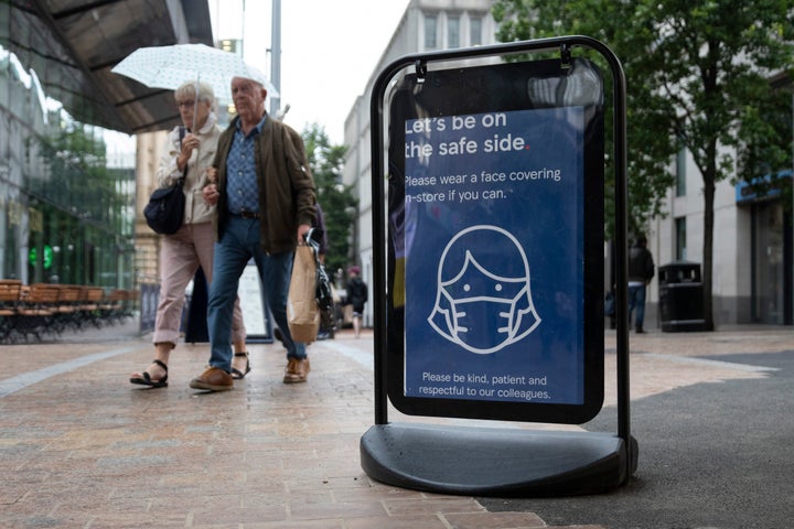 Shoppers pass a sign encouraging people to wear masks to reduce transmission of the coronavirus outside a Tesco supermarket