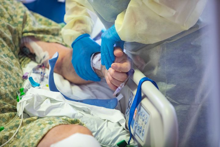 In this file photo from August 2021, a nurse holds the hand of a COVID-19 patient in the Medical Intensive care unit at St. Luke's Boise Medical Center in Boise, Idaho. 