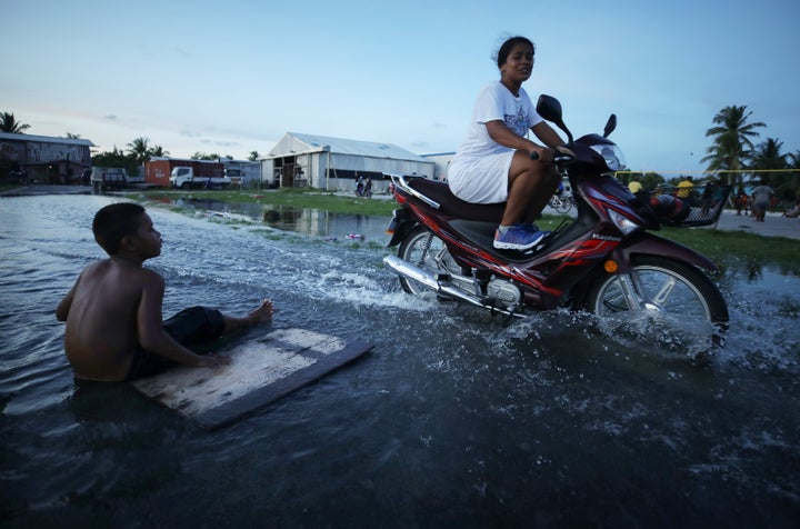 A woman rides her scooter through floodwaters occurring around high tide in a low-lying area near the airport in 2019 in Funafuti, Tuvalu. The South Pacific island nation of about 11,000 people has been classified as "extremely vulnerable" to climate change by the United Nations Development Program. 