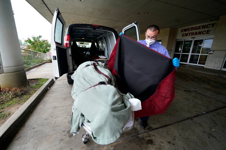 In this August 18, 2021 file photo, an employee of a local funeral home covers the body of a patient who died of COVID-19