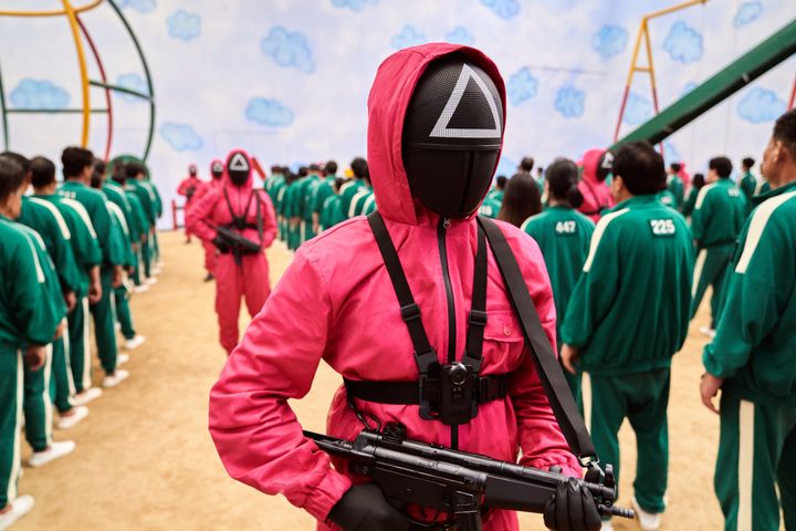 参加者を監視するゲームのスタッフは、ショッキングピンクの作業服に仮面をかぶっている。
