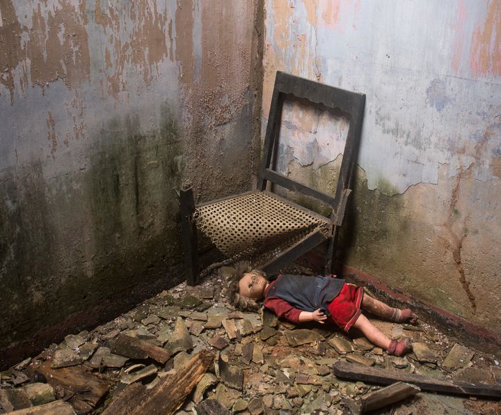 A doll next to a chair in an abandoned house.