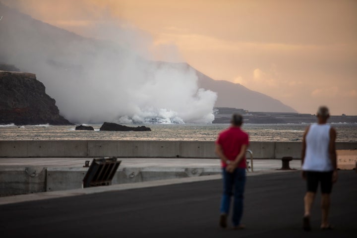 Varios habitantes observan, a lo lejos, la caída de lava en el mar