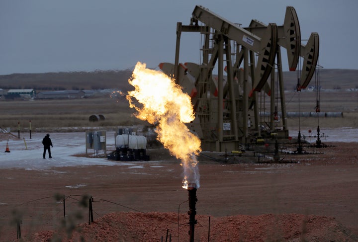 In this Oct. 22, 2015, file photo, workers tend to oil pump jacks behind a natural gas flare near Watford City, North Dakota. 