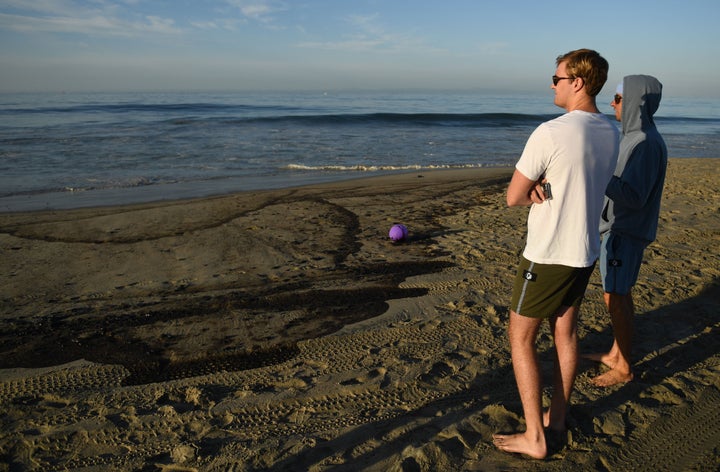 Surfers that planned on surfing look at oil on the beach in Huntington Beach, California on October 3, 2021. (Photo by PATRIC