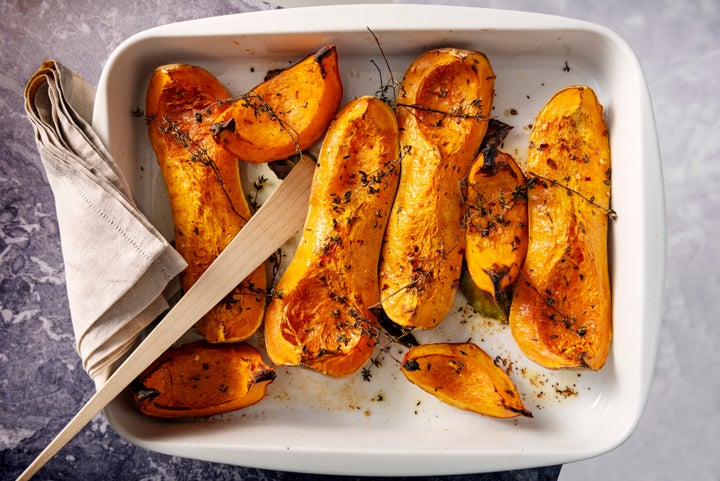 Dish of freshly roasted Butternut squashes cooked until they are soft, with thyme, bay leaves and olive oil. Colour, horizontal with some copy space.