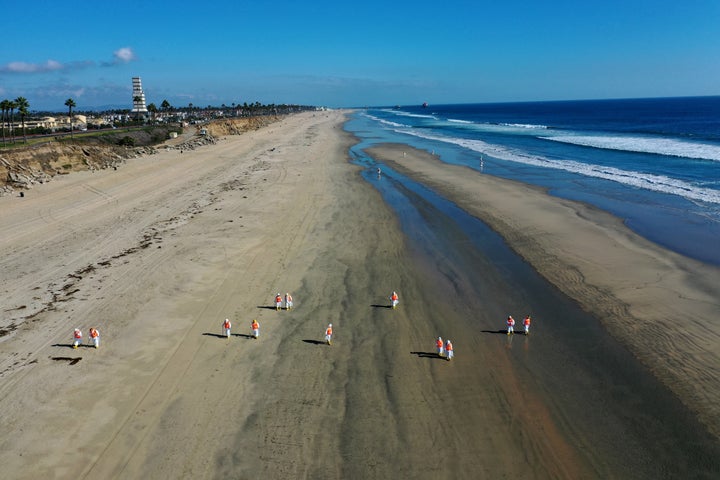 Environmental cleanup crews pick oil chucks off Huntington Dog Beach in Huntington Beach, California.