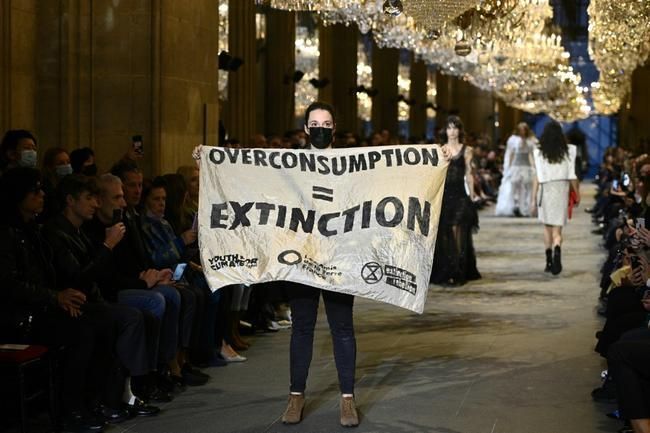 Ακτριβίστρια κρατάει πανό που γράφει «Υπερκατανάλωση = Αφανισμός» στην πασαρέλα του Louis Vuitton
