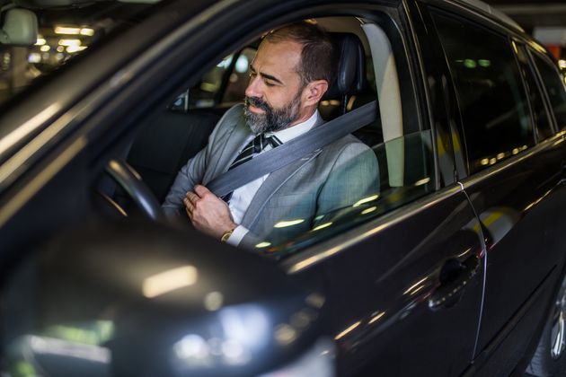 Businessman sitting in his car and adjusting his seat belt. Safety