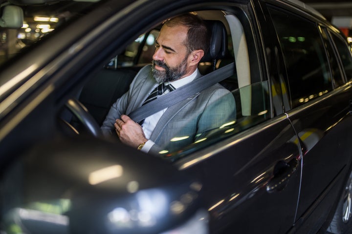 Businessman sitting in his car and adjusting his seat belt. Safety first.