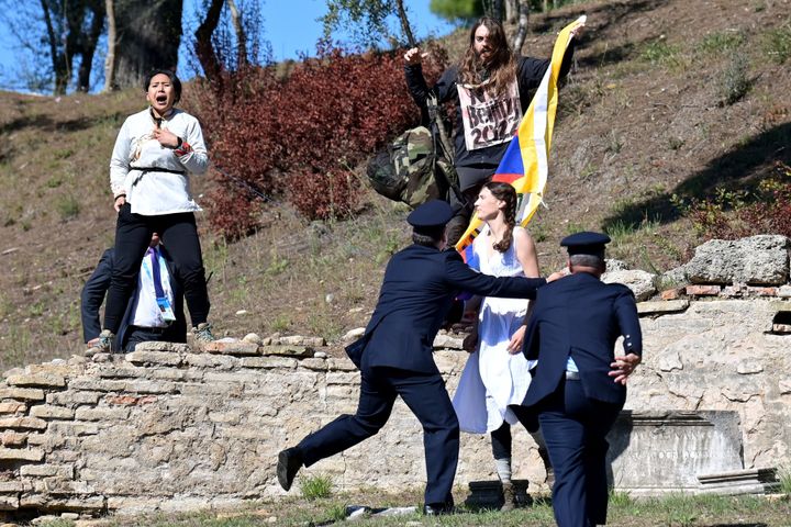 Security officers stop three protesters holding a banner and a Tibetan flag as they crash the flame lighting ceremony for the Beijing 2022 Winter Olympics at the Ancient Olympia archeological site.