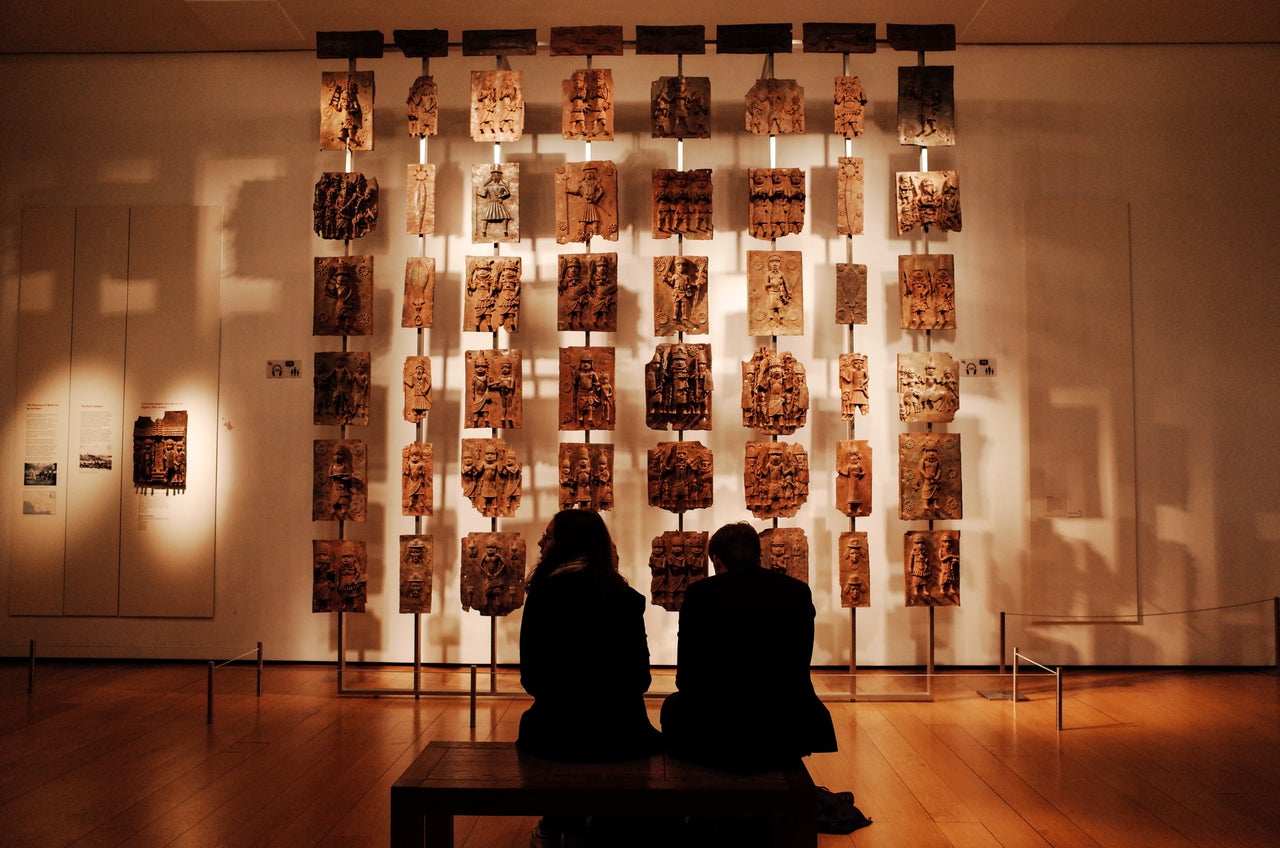 Visitors sit before the contentious Benin plaques exhibit (more commonly known as the Benin bronzes) at the British Museum in London.