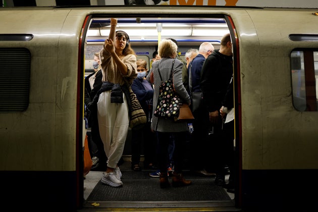 Commuters, some wearing face coverings to help prevent the spread of coronavirus, wait for the
